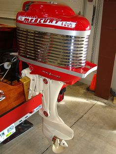 a red and white boat engine sitting on top of a wooden box in a garage