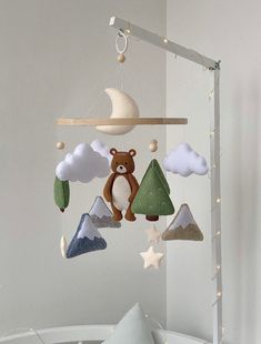 a baby crib mobile with a teddy bear hanging from it's side and mountains in the background