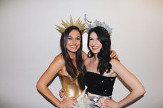 two women standing next to each other in front of a white wall wearing crowns and dresses