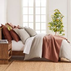 a bed with two pillows and blankets on top of it in front of a window