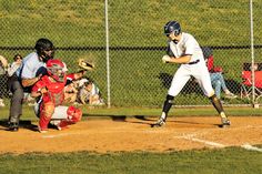 a baseball player holding a bat on top of a field next to home plate in front of a catcher and an umpire