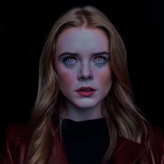 a woman with long blonde hair and blue eyes wearing a red leather jacket is looking at the camera