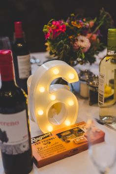 a table topped with wine bottles and glasses filled with liquid next to a light up number 6