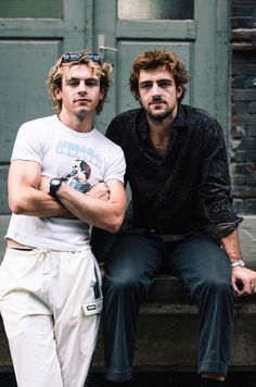 two men sitting on a bench with their arms crossed