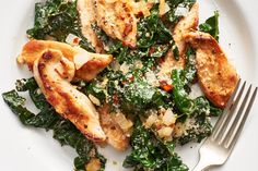 a white plate topped with chicken and greens next to a fork on top of a table