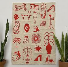 a red and white wall hanging on the side of a wall next to potted plants