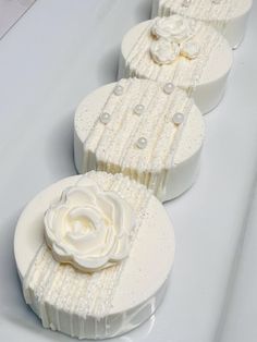 three cakes with white frosting and flowers on them sitting side by side in a row