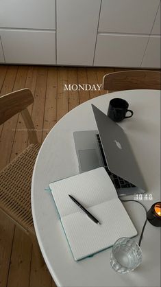 a laptop computer sitting on top of a white table next to a cup and pen