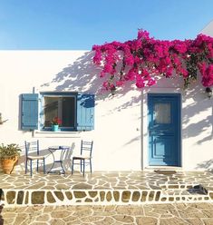 a white house with blue shutters and pink flowers