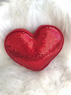 a red sequin heart shaped pillow on white fur