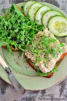 a green plate topped with an open face sandwich and cucumbers