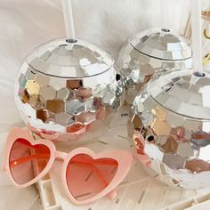 three mirrored balls with hearts on them sitting on a white surface next to a pair of sunglasses