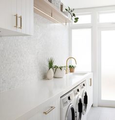 a washer and dryer in a white laundry room with plants on the shelf