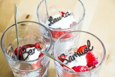 three glasses with strawberries and whipped cream on them sitting on a table next to each other