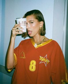 a woman drinking out of a cup while wearing a red and yellow shirt with the number 8 on it