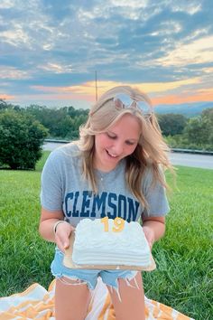 a young woman sitting on top of a blanket holding a cake