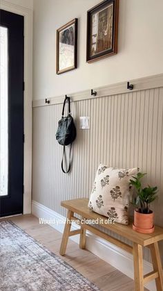 a wooden bench sitting in front of a black door next to a wall with pictures on it