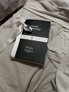 a book with a white ribbon on top of it sitting on a bed covered in sheets