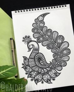 a drawing of a peacock on paper next to a pen and green leafy plant