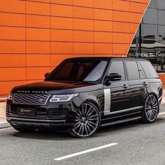 a black range rover parked in front of an orange building with white stripes on it