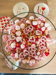 a glass bowl filled with valentine's day treats on top of a wooden table