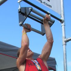 a man in red shirt holding up a metal pole above his head and lifting it with both hands