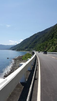 an empty highway next to the ocean with mountains in the background