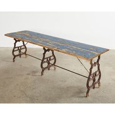 an old wooden table with iron legs and blue pattered paint on the top, sitting in a cement floor