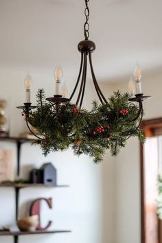 a chandelier hanging from the ceiling with candles and greenery on it's arms