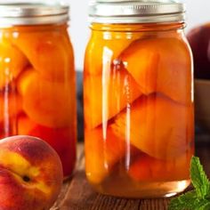 two jars filled with peaches on top of a wooden table