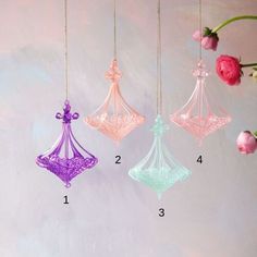 three different colored glass ornaments hanging from strings with flowers in the background on a pink wall