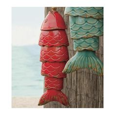 two red and green fish shaped ornaments hanging from a wooden fence next to the ocean