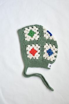 a crocheted green hat with white and blue flowers on the front, sitting on a white surface