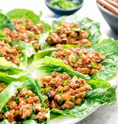 lettuce wraps filled with meat and vegetables on a plate next to chopsticks