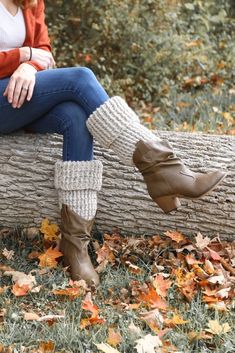 a woman sitting on top of a tree log wearing boots and leg warmers in the fall