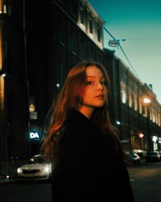 a woman standing in the middle of a street at night with her head turned to the side