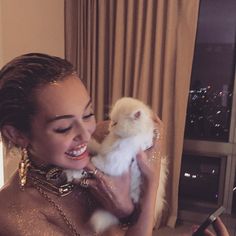 a woman holding a small white kitten in her hands and smiling at the camera while she holds it up to her face