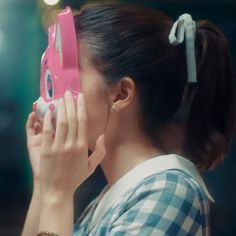 a woman holding up a pink camera to her face with one hand and looking into the mirror