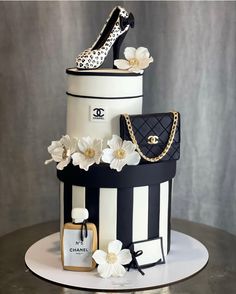 a black and white cake with high heel shoes, chanel bag and flowers on top