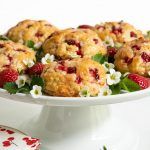 strawberry crumb muffins on a white cake plate with flowers and berries in the middle