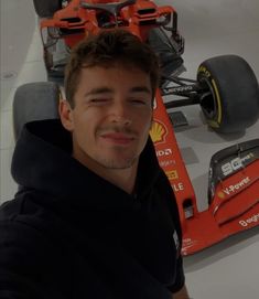 a man sitting in front of a race car with his eyes closed and smiling at the camera