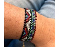 a person wearing a bracelet with multi colored beads on their arm and the other hand