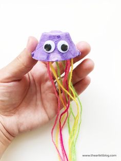 a hand holding a purple jellyfish with googly eyes