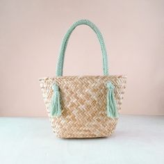 a woven bag with tassels on it sitting on a white table next to a pink wall