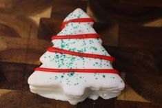 a white and green christmas tree shaped cookie on a cutting board with red ribbon around it