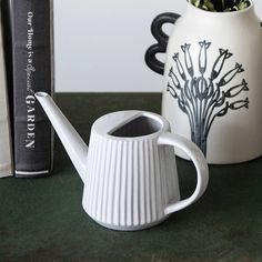 a white watering can sitting on top of a table next to a bookshelf