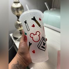 a person holding up a cup with mickey mouse designs on it and other items around the cup