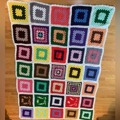 a colorful crocheted blanket is hanging on the wall in front of a wooden floor