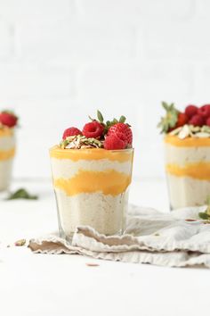 three desserts with strawberries and other toppings in small glass cups on a white table