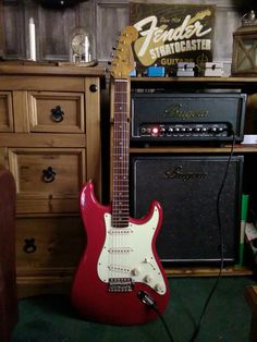 a red guitar sitting on top of a green carpeted floor next to a wooden dresser